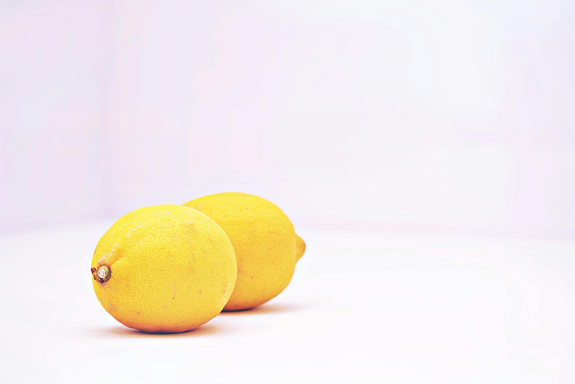 Two vibrant lemons against a minimalistic white background, symbolizing freshness and the gentle restart of sensual exploration