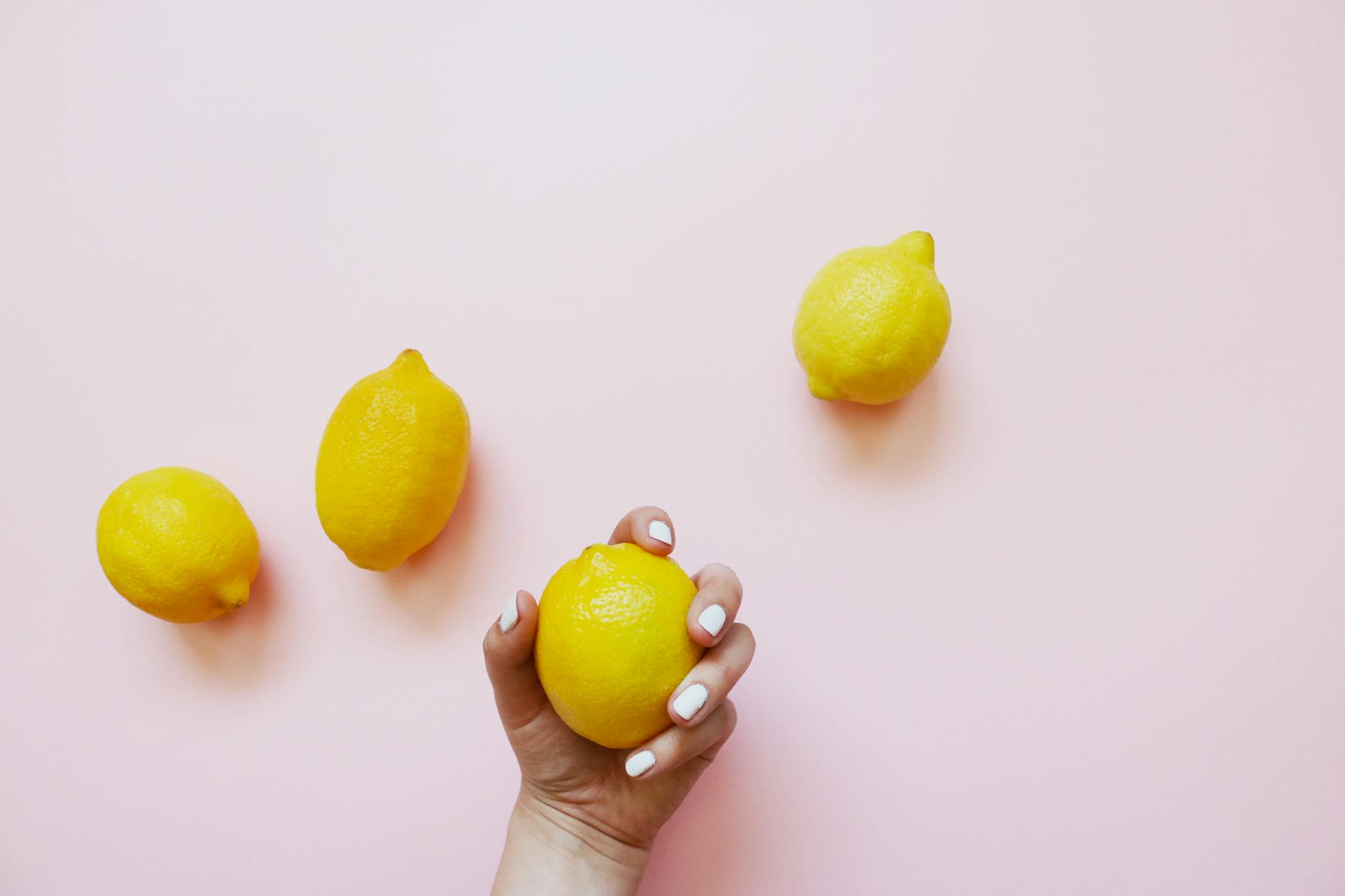 A hand holding a lemon on a soft pink background, symbolizing the citrus design of lemon clitoral vibrators
