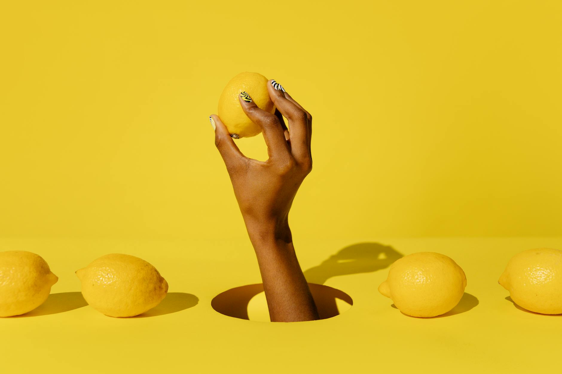 A hand holding a lemon against a vivid yellow background, symbolizing freshness and natural pleasure