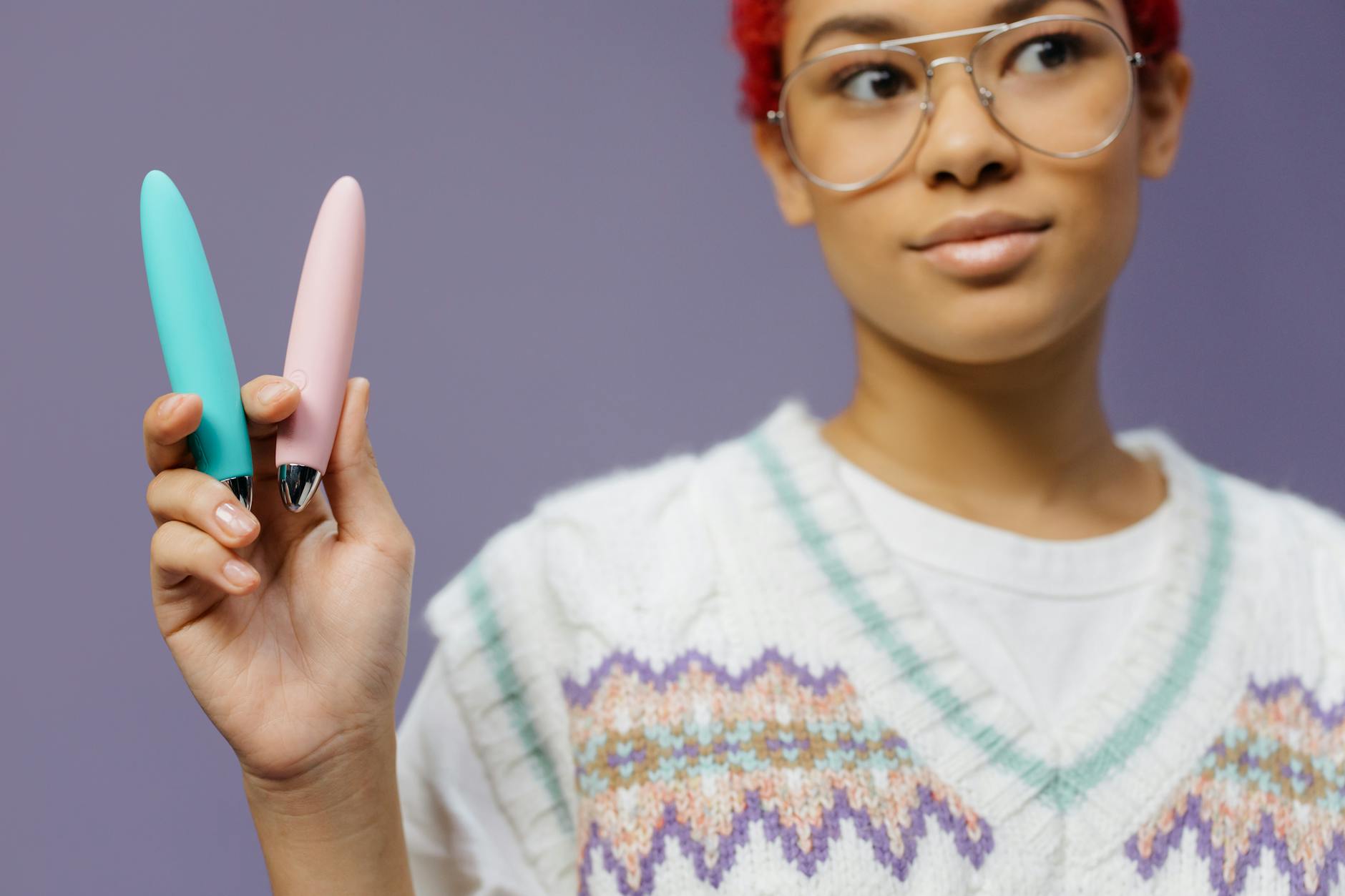 Two colorful clitoral vibrators held against a purple background, comparing modern toy designs