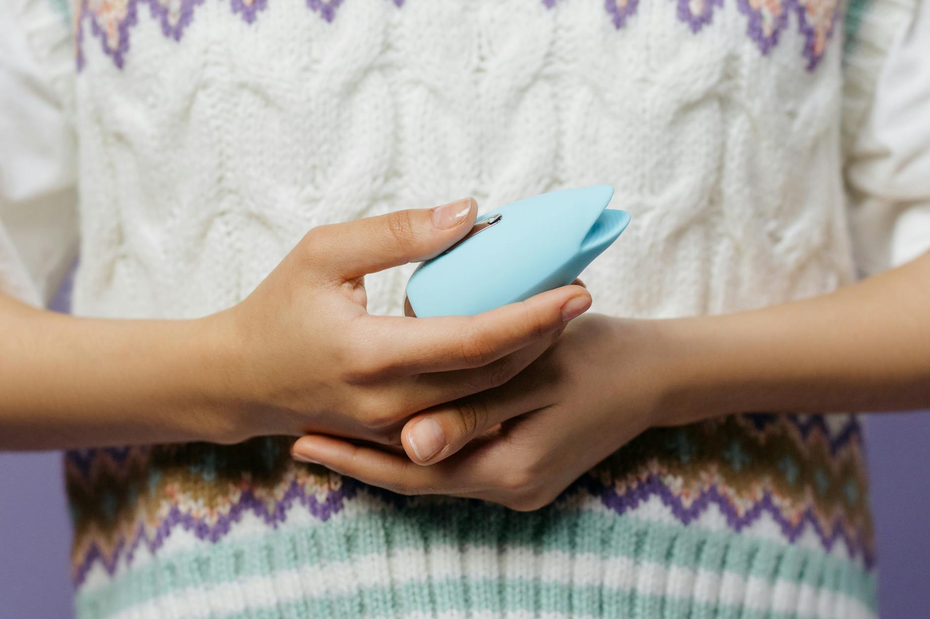 Close-up of hands holding a blue personal massager against a knitted sweater during recovery